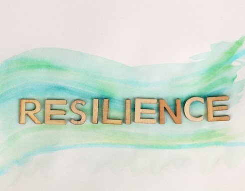 [Symbolbild zum Kurs "Gestärkt durch den Alltag - Resilienztraining für Ausbilder*innen und Lehrlinge"] Im Bild: Holzlettern auf pastellfarbenem Untergrund, die das Wort "Resilience" formen