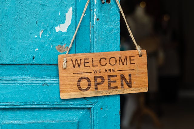 Willkommen im Team! Inklusives Onboarding für Lehrlinge. Im Bild: Holzschild mit der Aufschrift "Welcome - We are open"