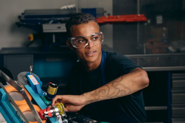 Bild eines jungen Mannes der mit Schutzbrille an einer Maschine arbeitet