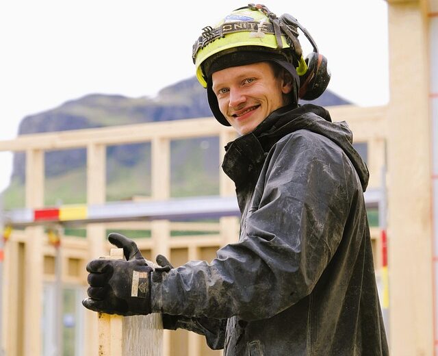 Bild eines jungen Mannes in Schutzkleidung der auf einer Bausstelle Holzteile hält