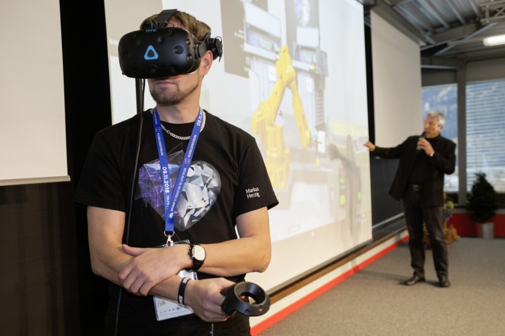 Bild von einer Person mit VR-Brille, im Hintergrund ein Redner bei einer Präsentation