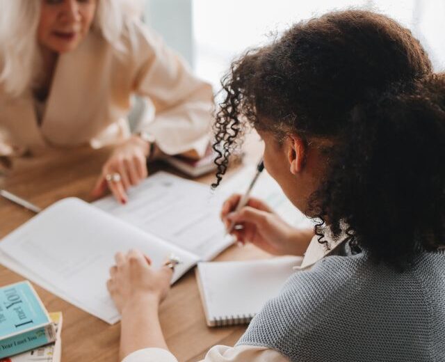 Bild von einer jungen und älteren Frau im Arbeitskontext, die gemeinsam Unterlagen bearbeiten
