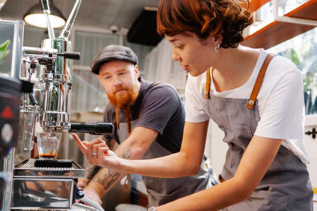 Junge Frau bedient eine Kaffeemaschine, ein älterer Kollege schaut ihr über die Schulter