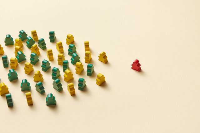 Bild von Spielfiguren aus Holz, von denen eine andersfarbige Figur rechts am Rand steht