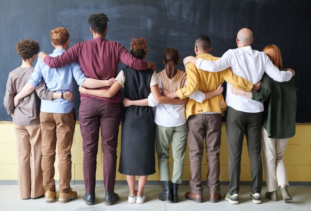 Gruppe von jungen Menschen die alle mit dem Rücken zur Kamera stehen und einander die Arme um die Schultern legen